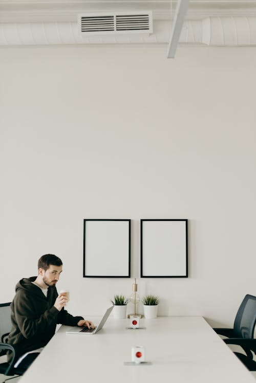 Man In Black Hoodie Using Laptop While Drinking Coffee