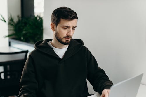 Man in Black Zip Up Jacket Standing Near White Wall