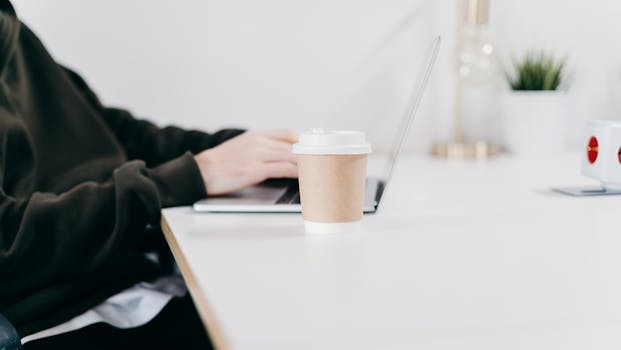 A person working on a laptop in a home office with a coffee cup on the desk, creating a minimalist workspace feel.