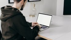 一个年轻男子穿着连帽衫，在现代家庭办公环境中用笔记本电脑工作