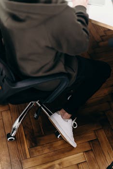 Man in hoodie working at desk with parquet flooring and white sneakers