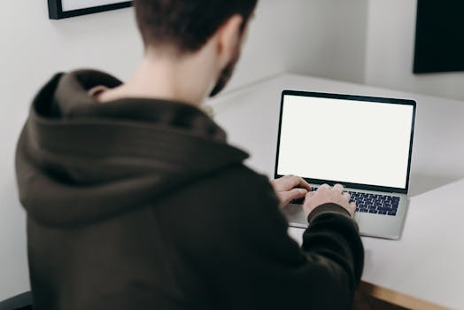 Man working on a laptop with a blank screen in a minimalist home office setting.