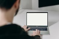 一个身着连帽衫的男人，正在一个干净简约的室内工作空间里，对着一台屏幕空白的笔记本电脑工作