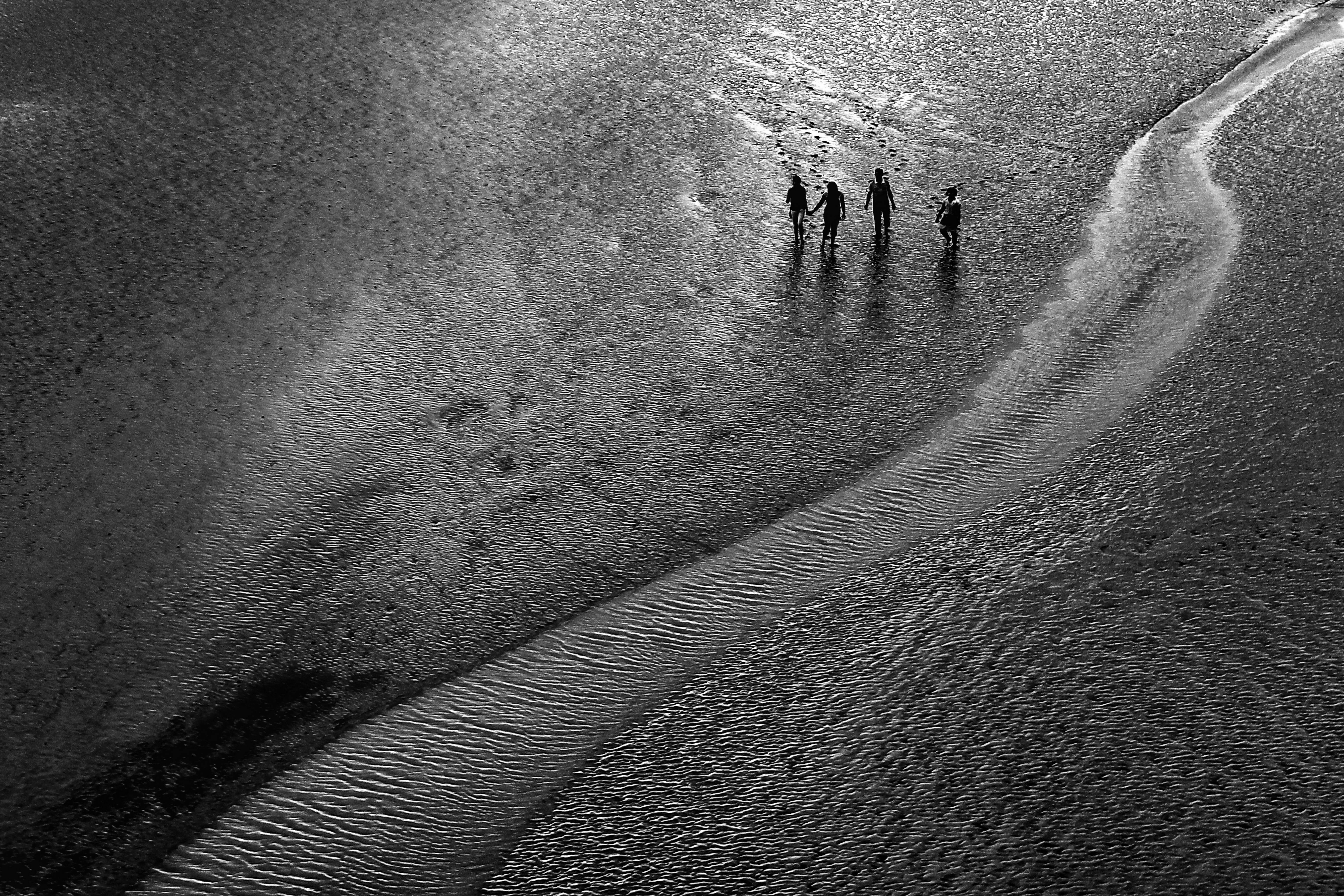 Monochrome aerial view of people walking along a beach path, evoking adventure.