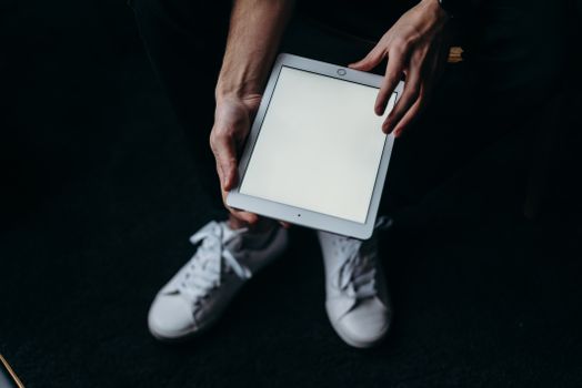 Close-up of hands holding a blank tablet screen with white sneakers. Ideal for tech themes.