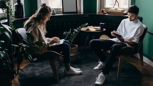 Two young adults working in a stylish home office, using laptops and tablets for remote work.