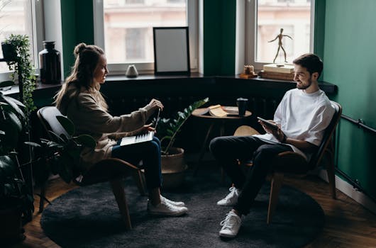 Young professionals working in a cozy home office environment, discussing projects over laptops.