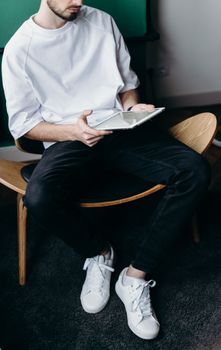 一个穿着随意的男人坐在家里的现代椅子上，用着平板电脑