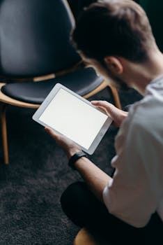 A young man seated indoors using a tablet, perfect for business and lifestyle themes.