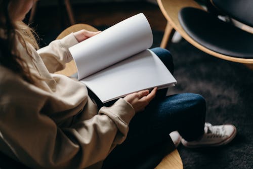 Free Person in Blue Denim Jeans Holding White Book Stock Photo