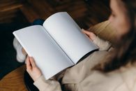A woman is sitting indoors holding and reading a blank open notebook.