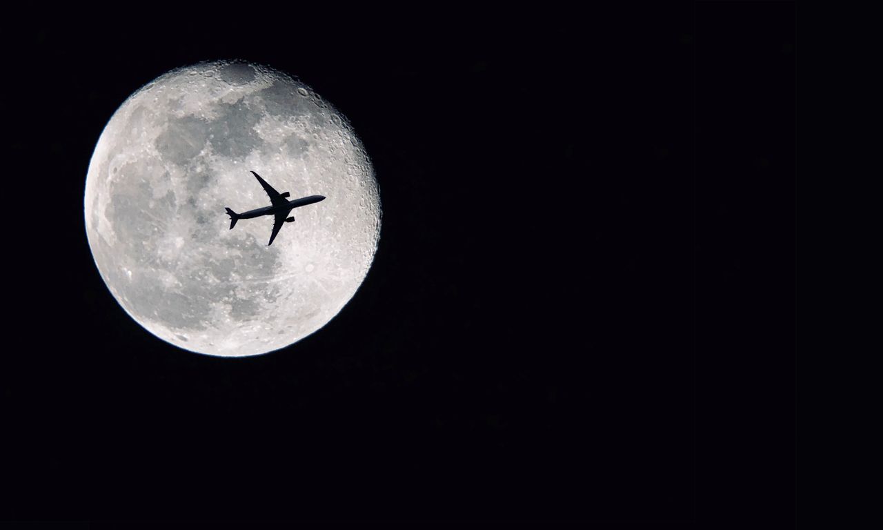 dramatic airplane silhouette crossing in front of a detailed full moon