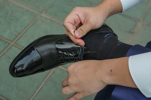 Person Tying Black Leather Shoe