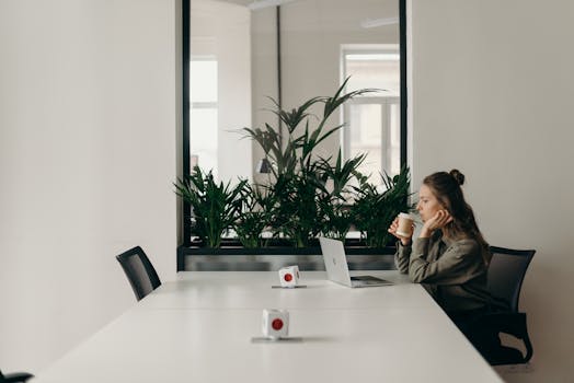 Woman working on laptop while drinking coffee in a modern, minimalist office setting.