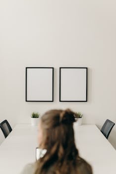 A minimalist workplace with blank frames on the wall and a person sitting at a table.