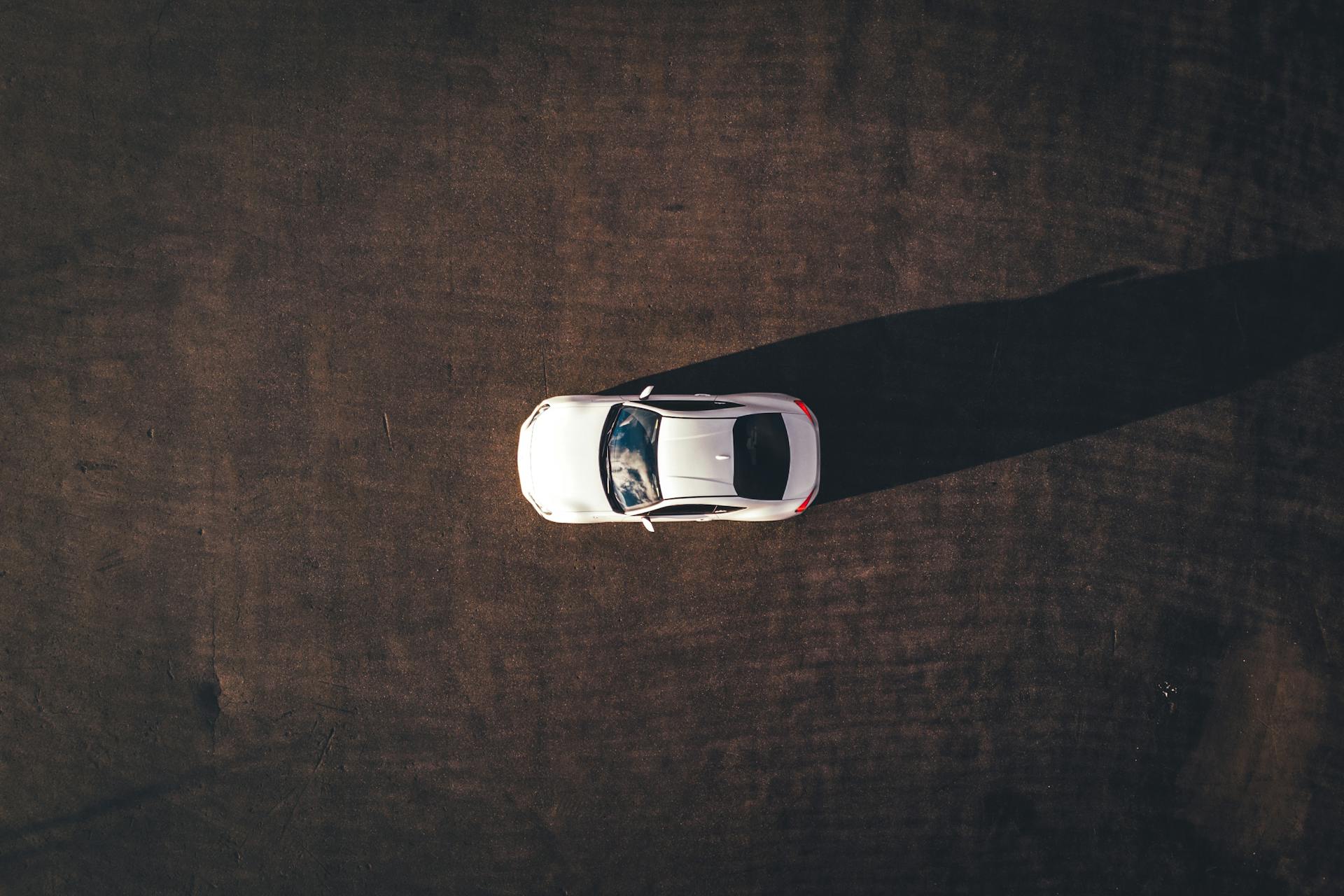 Top-down drone shot of a white sports car casting a shadow on asphalt