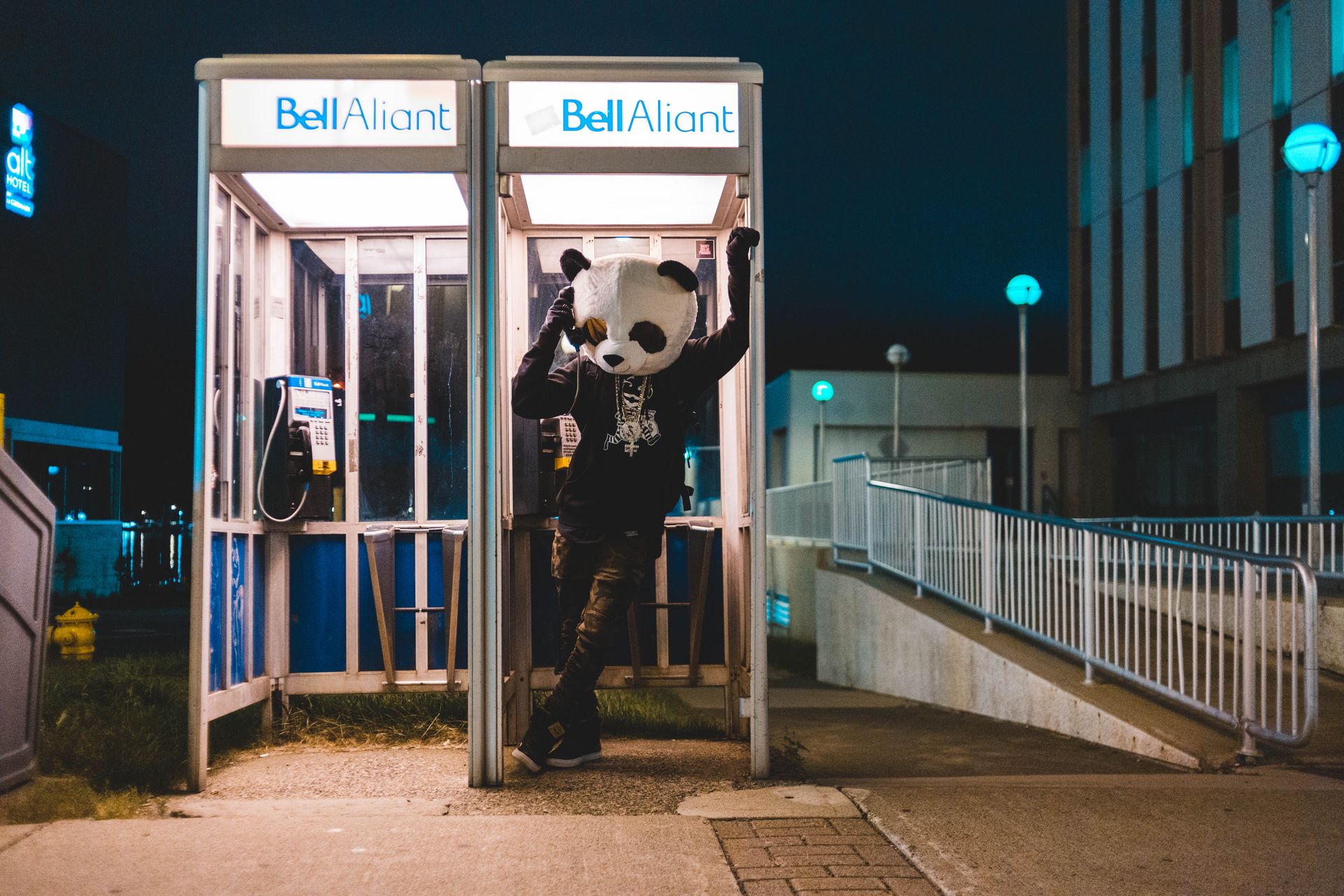 Man in Black and White Panda Costume Standing on Payphone Booth during Night Time