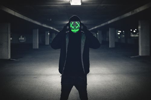 Free A person wearing a neon LED mask stands in a dimly lit underground parking lot, creating an eerie atmosphere. Stock Photo