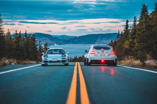Two sports cars on a scenic highway during sunset with a beautiful landscape.