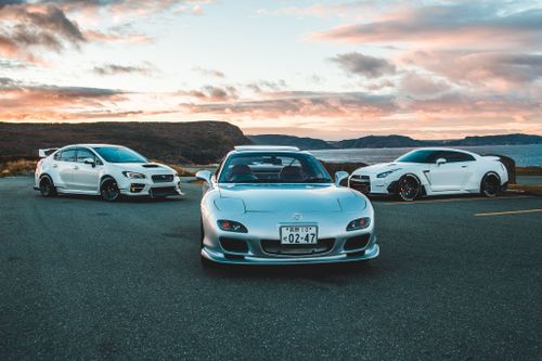 Free Three luxury sports cars parked outdoors with a stunning sunset backdrop. Stock Photo
