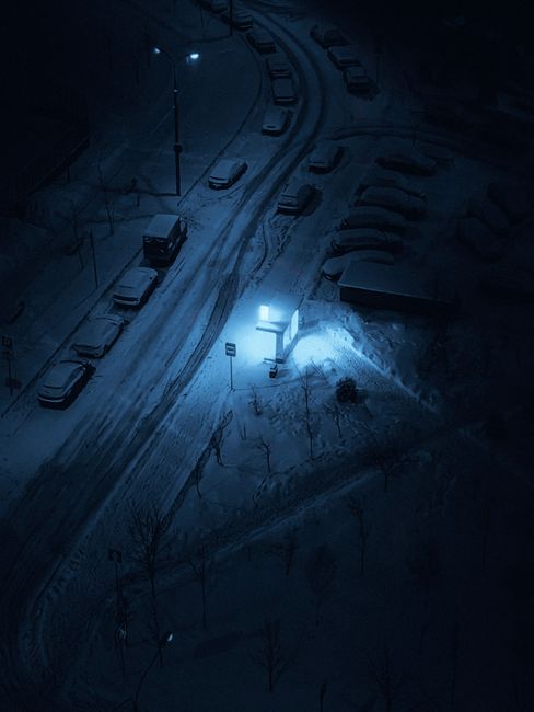 A high angle view of a snowy urban bus stop illuminated at night, creating an eerie winter scene.
