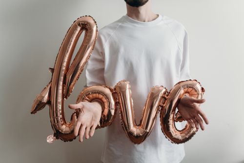 Free A man holding rose gold love balloons wearing a white t-shirt, showcasing minimalist love symbolism. Stock Photo