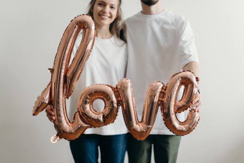 Free A couple in white t-shirts holds a metallic love balloon, symbolizing affection and joy. Stock Photo