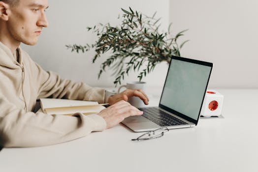 A young man focused on his laptop at a stylish home office desk with plants.