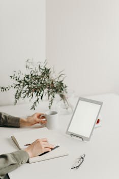 A minimalist home office setup with a blank screen tablet, coffee mug, and greenery.