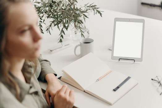 Minimalist home office setup with tablet, coffee mug, and open notebook on a white desk.