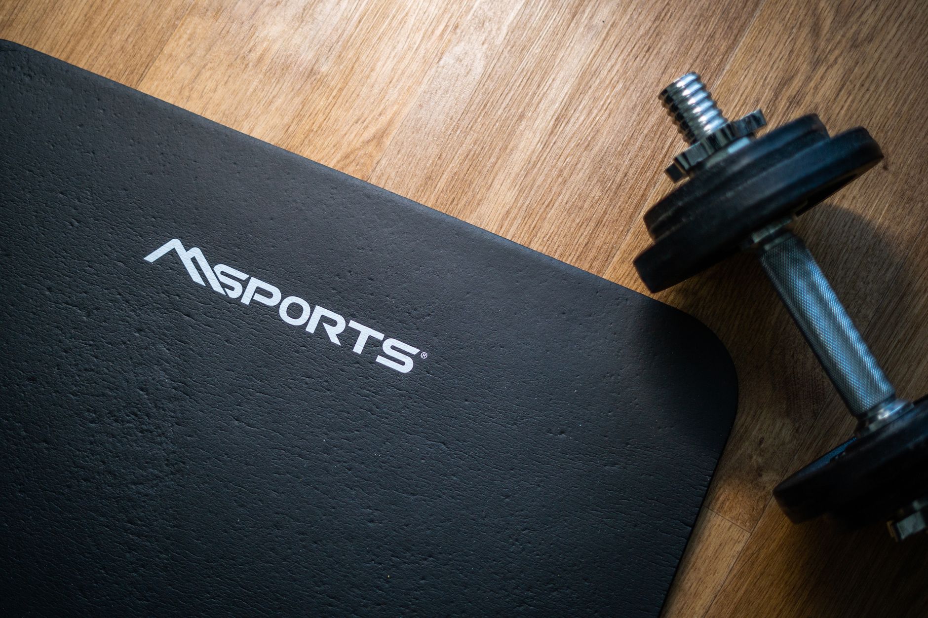 Flat lay of a gym mat and dumbbell on wooden floor, ideal for indoor workouts.