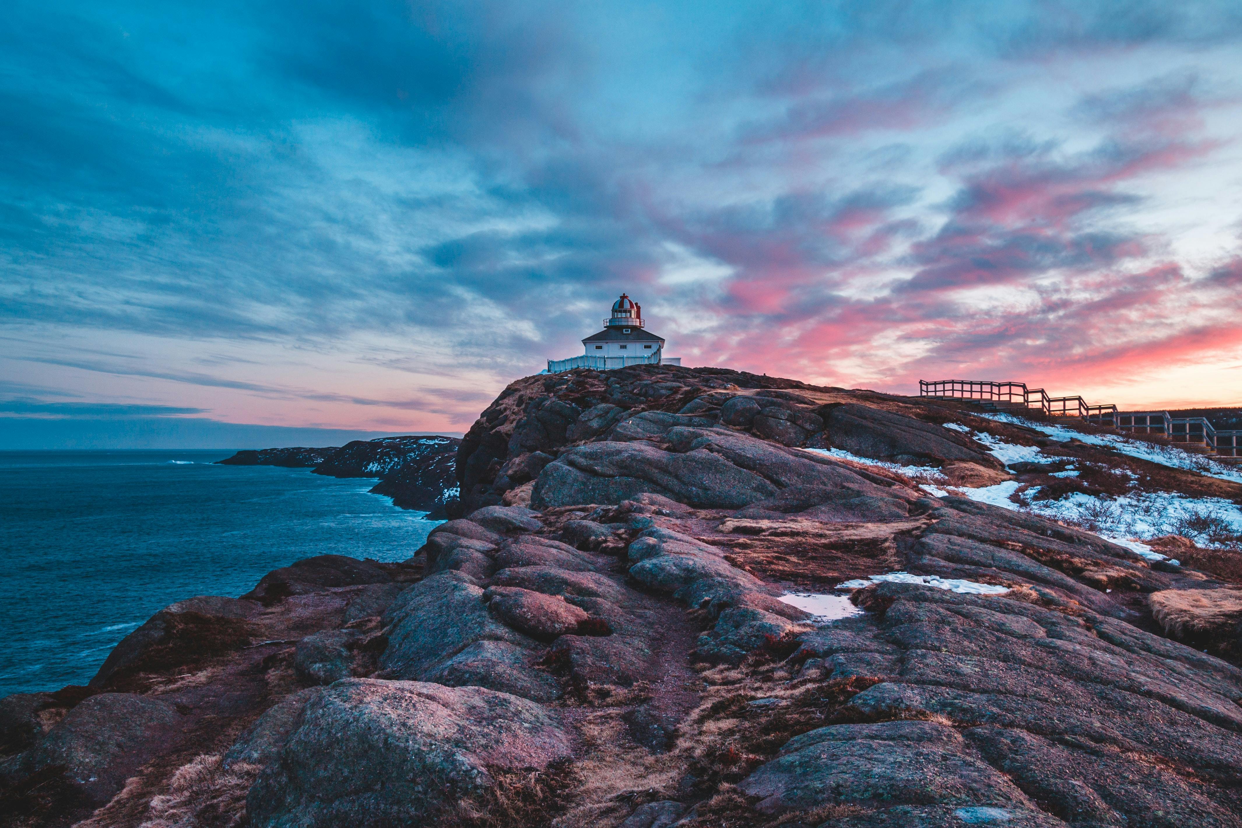 Lighthouse perched on rocky coast during a dramatic sunset with vibrant skies.