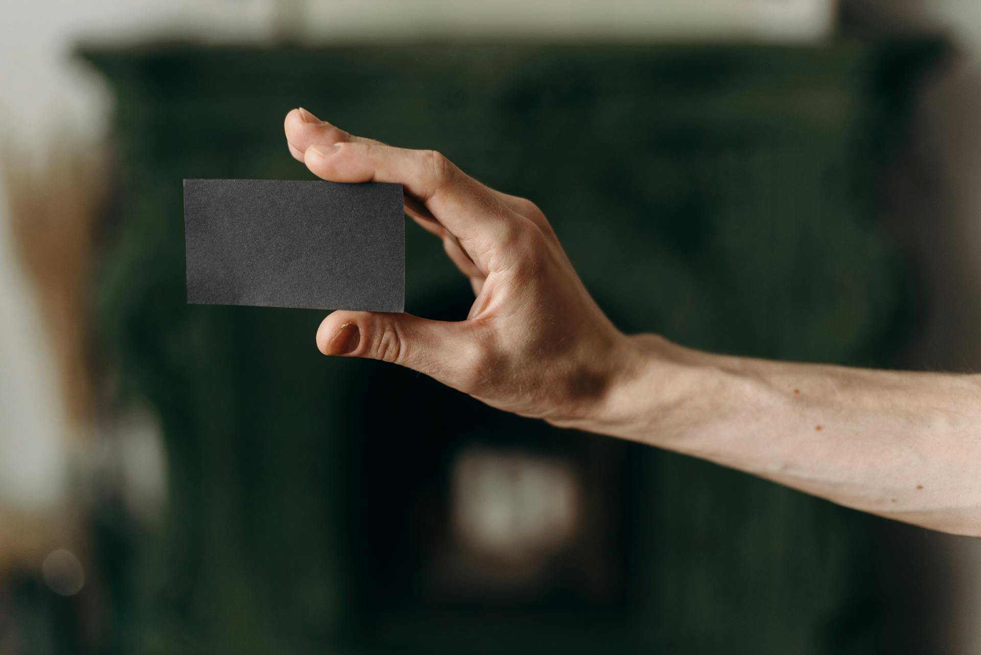 A hand holding a blank black card with a blurred background, perfect for mockup or copy space.