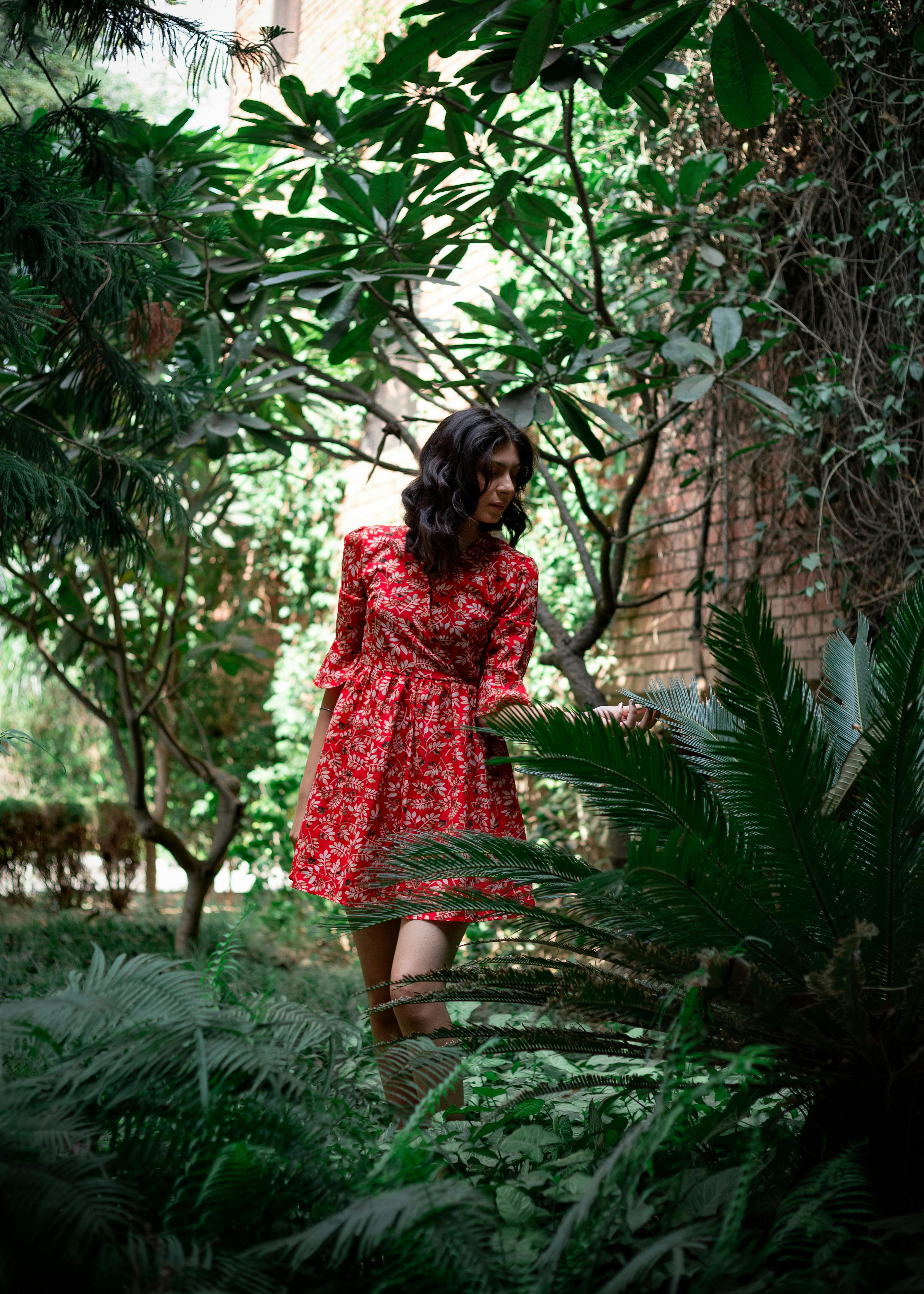 A woman in a red floral dress explores a lush garden, surrounded by verdant plants.