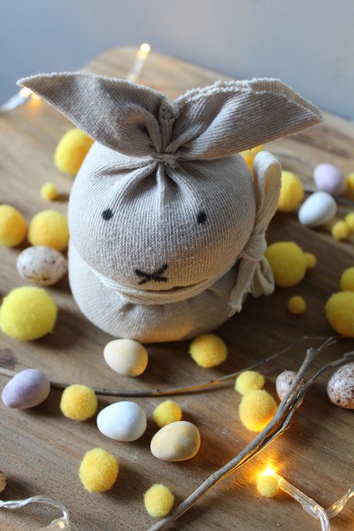 Free From above of cute handmade Easter Bunny placed on wooden table near scattered decorative eggs and glowing garland Stock Photo