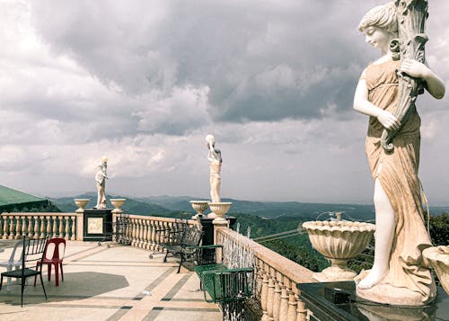 Spacious cafe terrace with antique marble statues and breathtaking view of green mountainous terrain against cloudy sky