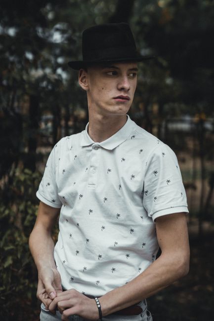 Stylish young man wearing a black fedora looking away outdoors, exuding individuality.