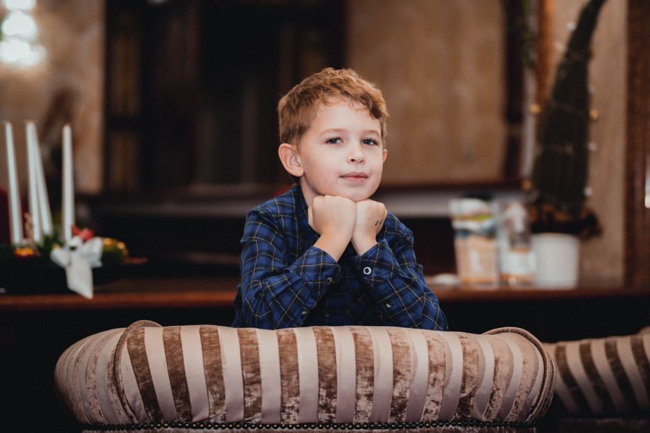 A young boy in a plaid shirt poses charmingly indoors, showcasing his personality on a couch.