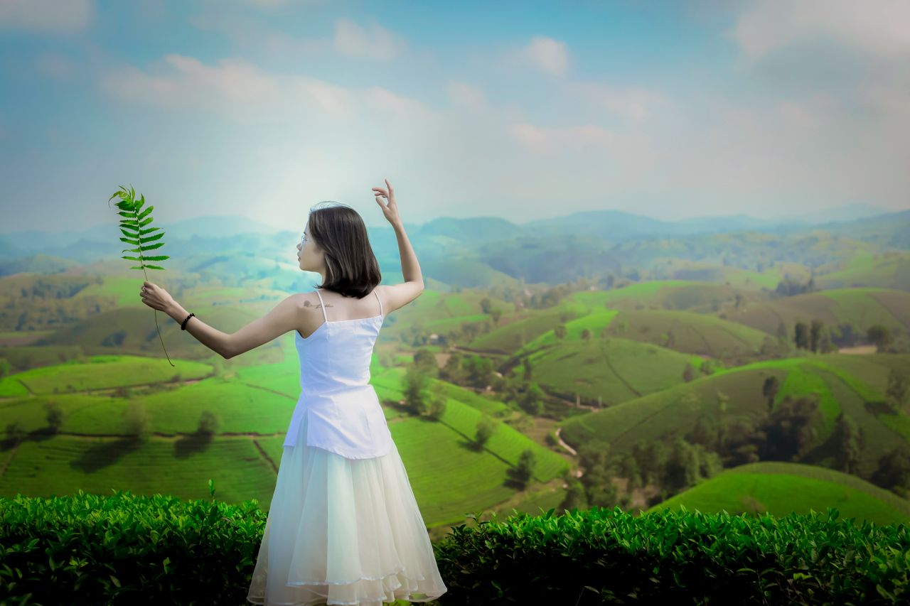 woman in white dress posing with branch in hand on lush green hills