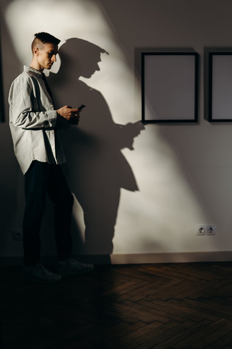 Man In White Dress Shirt And Black Pants Standing Beside White Wall