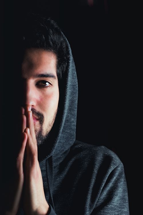 Free Introspective close-up portrait of a bearded man in a hoodie with a dark background. Stock Photo