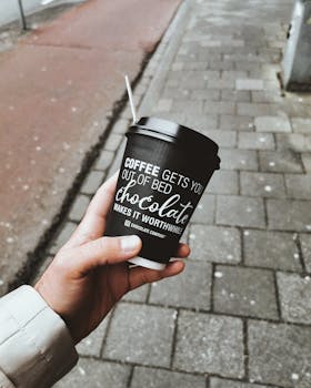 Hand holding a disposable coffee cup with a motivational message on an urban street.