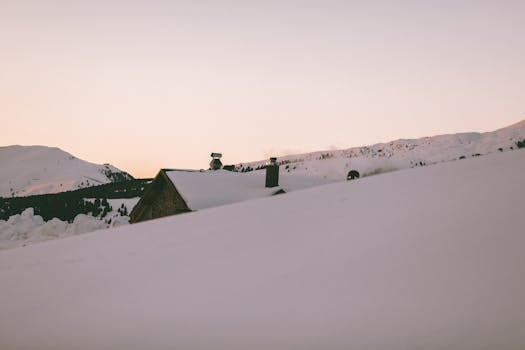 Tranquil mountain scenery with snow-covered house at sunset in winter.