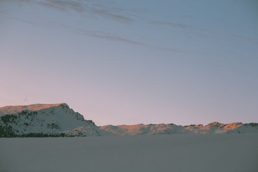 Tranquil snowy mountain range at dawn with soft pastel sky.