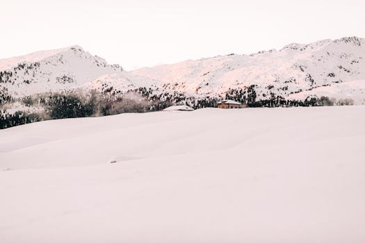 Idyllic winter scene with snow-covered mountains and a solitary cabin at sunrise.
