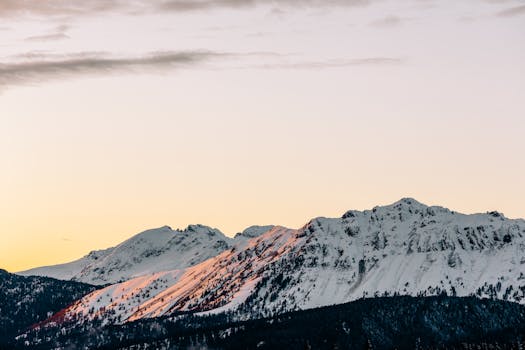 Beautiful snow-covered mountain range illuminated by sunset, capturing serene and tranquil winter scenery.