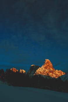 Stunning alpine mountain peak illuminated at twilight with snow-covered landscape.