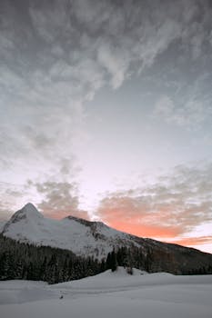 Beautiful snow-capped mountains under a pink sunrise sky, capturing serene winter landscape.