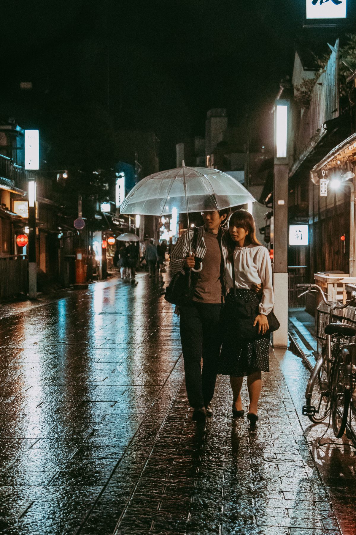 A couple walking under an umbrella on a rainy Kyoto street