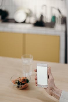 Minimalist home office setting with a smartphone, glass of water, and salad bowl on a wooden table.
